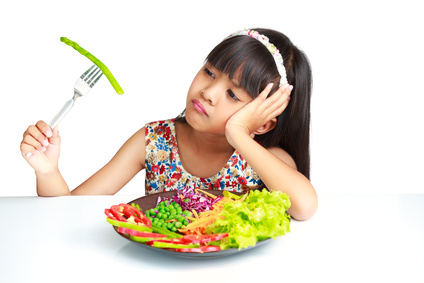 Little asian girl with expression of disgust against broccoli, Isolated over white